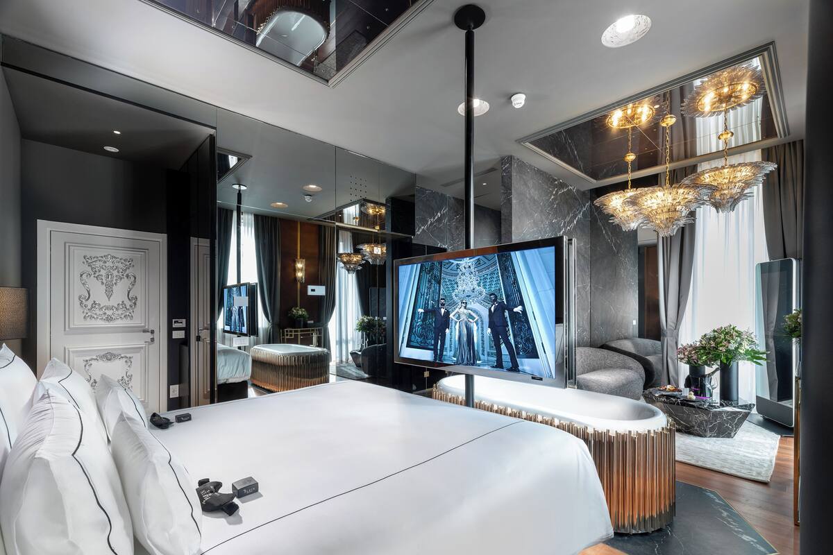 A modern bedroom with a large bed, a TV, and a chandelier.