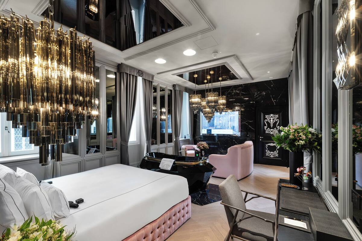 A modern hotel room with a large bed, a sitting area with a chair, a desk, and a TV.