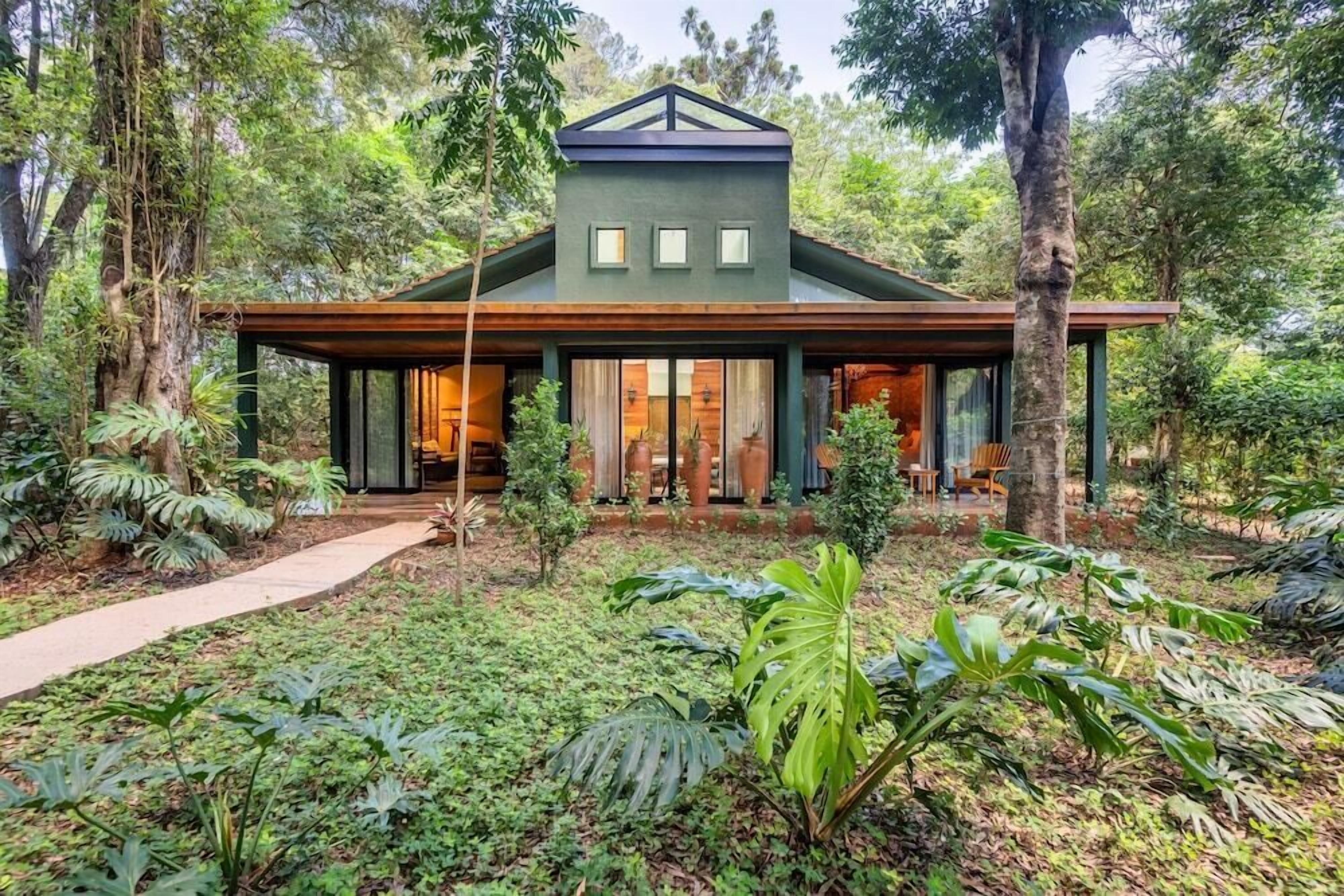 Uma casa moderna com varanda frontal espaçosa, cercada por vegetação exuberante e árvores.
