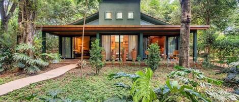 Ein modernes Haus mit einer breiten Veranda, umgeben von üppigem Grün und Bäumen.