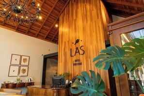 A reception desk with a wooden backdrop, a chandelier, framed artwork, and a plant.