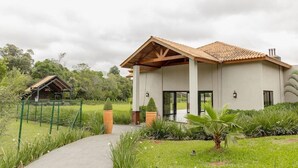 A modern building with a covered entrance, a fenced garden, and a small structure in the background. - Las Hotel Boutique (Foz do Iguaçu)