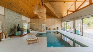 A modern indoor swimming pool with wooden beams, a stone sculpture, and a view of greenery outside. - Las Hotel Boutique (Foz do Iguaçu)