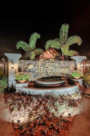 A hotel entrance with a stone facade, a fountain, and various plants.