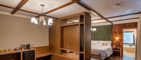 Una habitación de hotel con techo de madera, una cama, zona de estar y una pequeña kitchenette.
