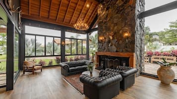 Amplia sala de estar con chimenea, sofás de cuero y un gran ventanal con vistas a un jardín.