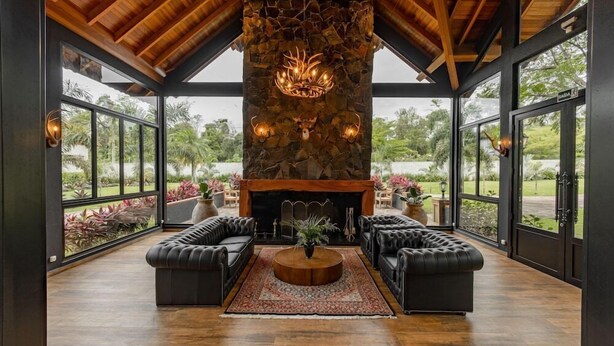 A spacious living area with a stone fireplace, leather sofas, and large windows offering a view of the outdoors. - Las Hotel Boutique (Foz do Iguaçu)