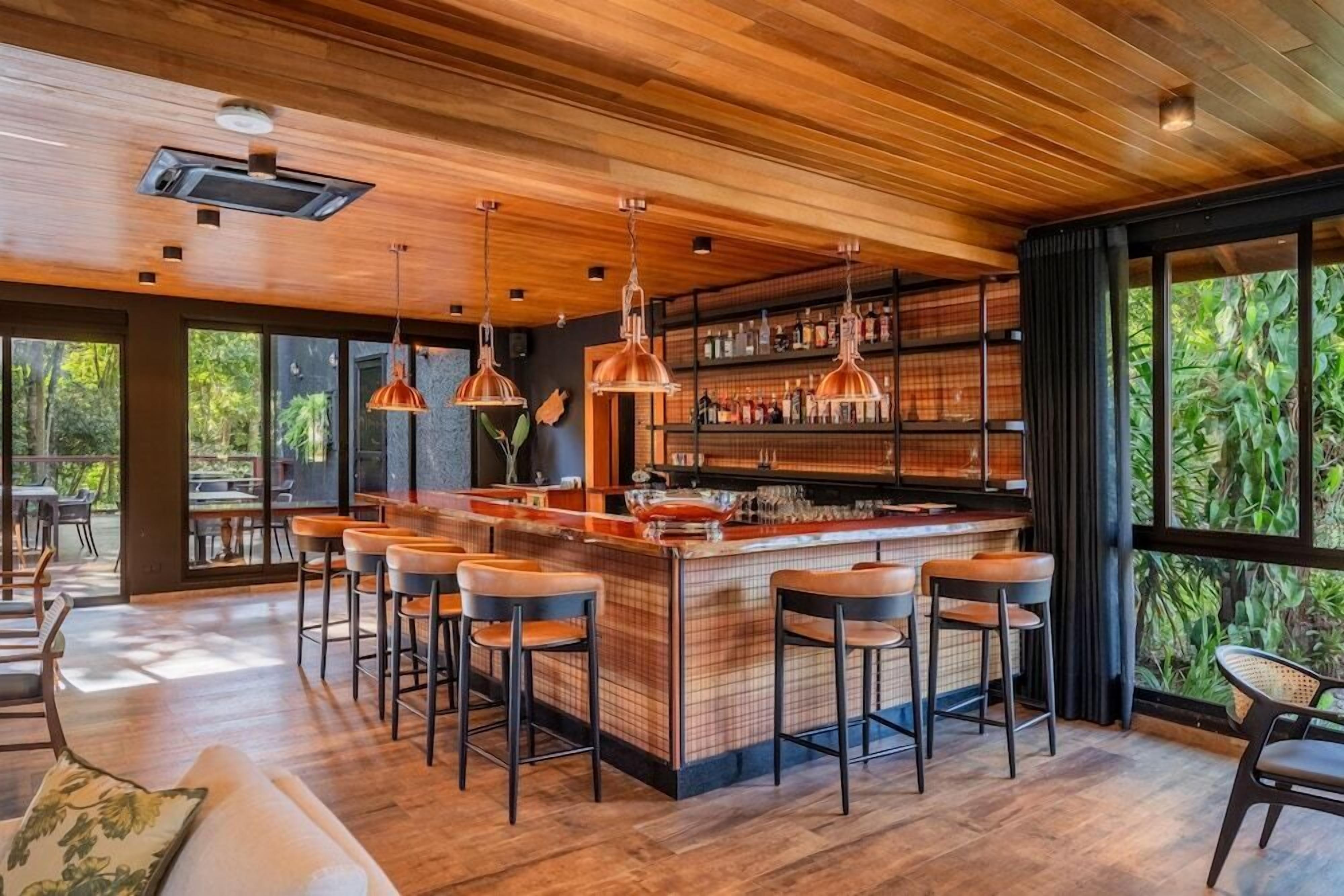 Uma área de bar moderna com teto de madeira, banquetas e balcão.