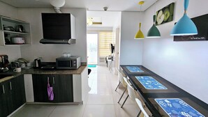 A modern kitchen with a microwave, kettle, and dish rack. There are hanging lights and a view of the city through the window. - Birchtower by Jeizel Manila City By Zuzu (Manila)