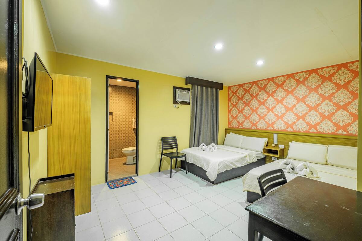 A hotel room with a bed, a desk, a chair, a TV, and a bathroom visible through an open door.