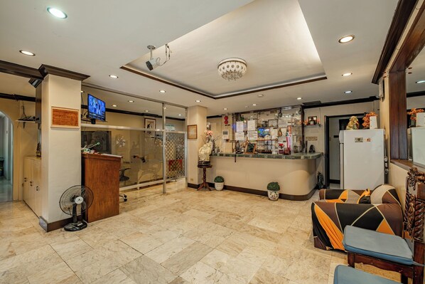 A hotel lobby with a reception desk, a TV, and a seating area with a sofa and chairs.