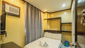 A hotel room with a bed, a small table, a trash bin, and an air conditioning unit. - Hotel Juliano By Zuzu (Manila)