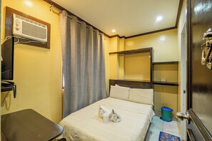 A hotel room with a bed, a small table, a trash bin, and an air conditioning unit. - Hotel Juliano By Zuzu (Manila)