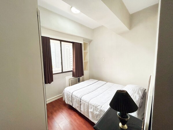 A bedroom with a bed, a nightstand, a window with curtains, and a radiator. - Sunette Tower Suites Makati City Center By Zuzu (Makati)