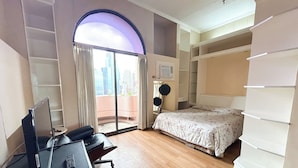 Une chambre à coucher comprenant un lit, un bureau avec un ordinateur, une chaise, une armoire et une vue sur la ville par le biais d’une grande fenêtre.