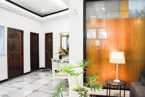 A hotel lobby with a marble floor, wooden doors, a white reception desk, a potted plant, a lamp, and a grey armchair. - Sunette Tower Suites Makati City Center By Zuzu (Makati)
