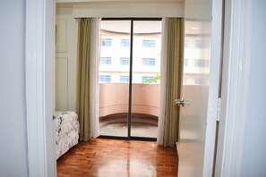 A room with a wooden floor, a bed with a floral bedspread, and a sliding glass door leading to a balcony. - Sunette Tower Suites Makati City Center By Zuzu (Makati)