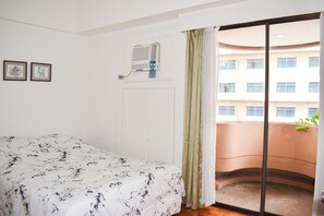 Un dormitorio con cama, aire acondicionado, ventana con cortinas y balcón con planta.