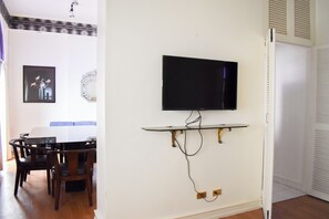A dining area with a table and chairs, a mounted television, and a wall-mounted shelf. - Sunette Tower Suites Makati City Center By Zuzu (Makati)