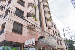 Un edificio de varios pisos con balcones, un letrero que dice 'Sunette Tower Condo Suites' y varios letreros, incluyendo 'HANADY 2'.