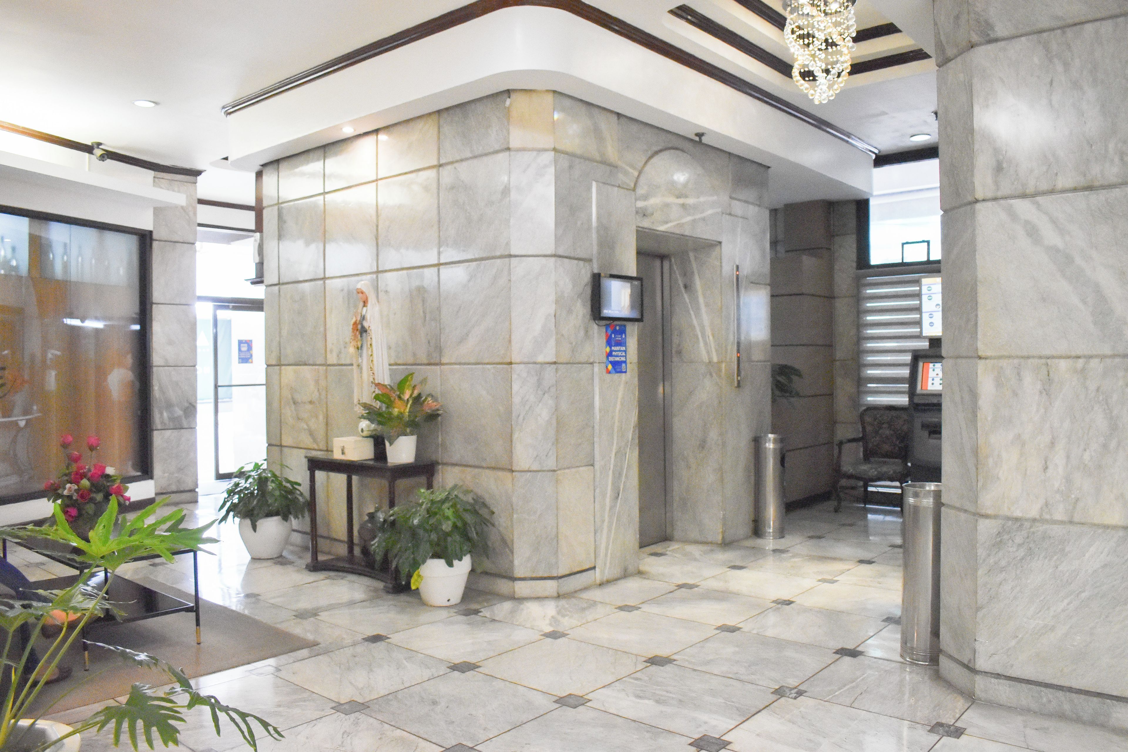 A lobby with marble flooring, a reception desk, potted plants, and a modern chandelier.