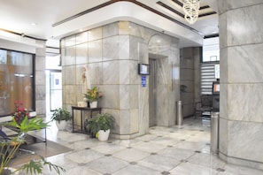 Um hall com piso de mármore, um balcão de recepção, plantas em vasos e um lustre moderno.