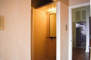 Un pasillo estrecho con un espejo y luces, que conduce a una zona de cocina con un refrigerador.