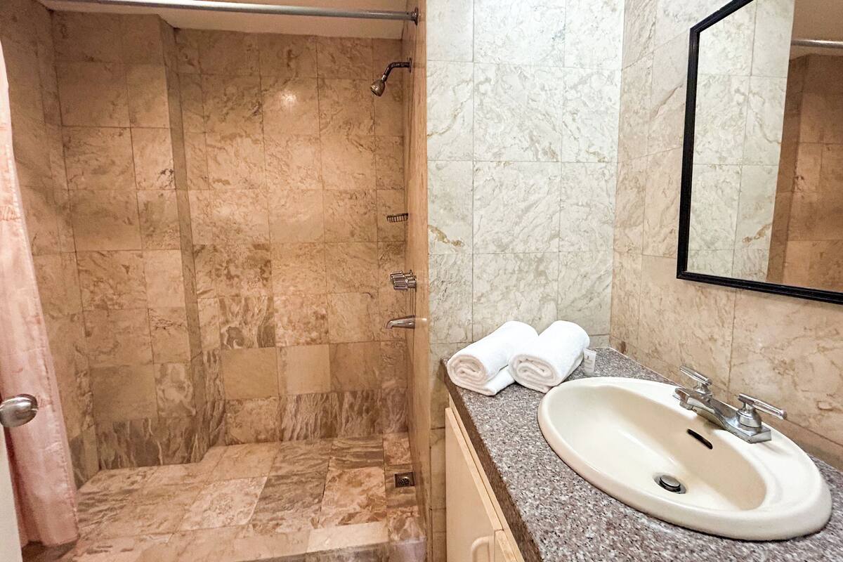 A bathroom with a marble shower, a sink, and a mirror.