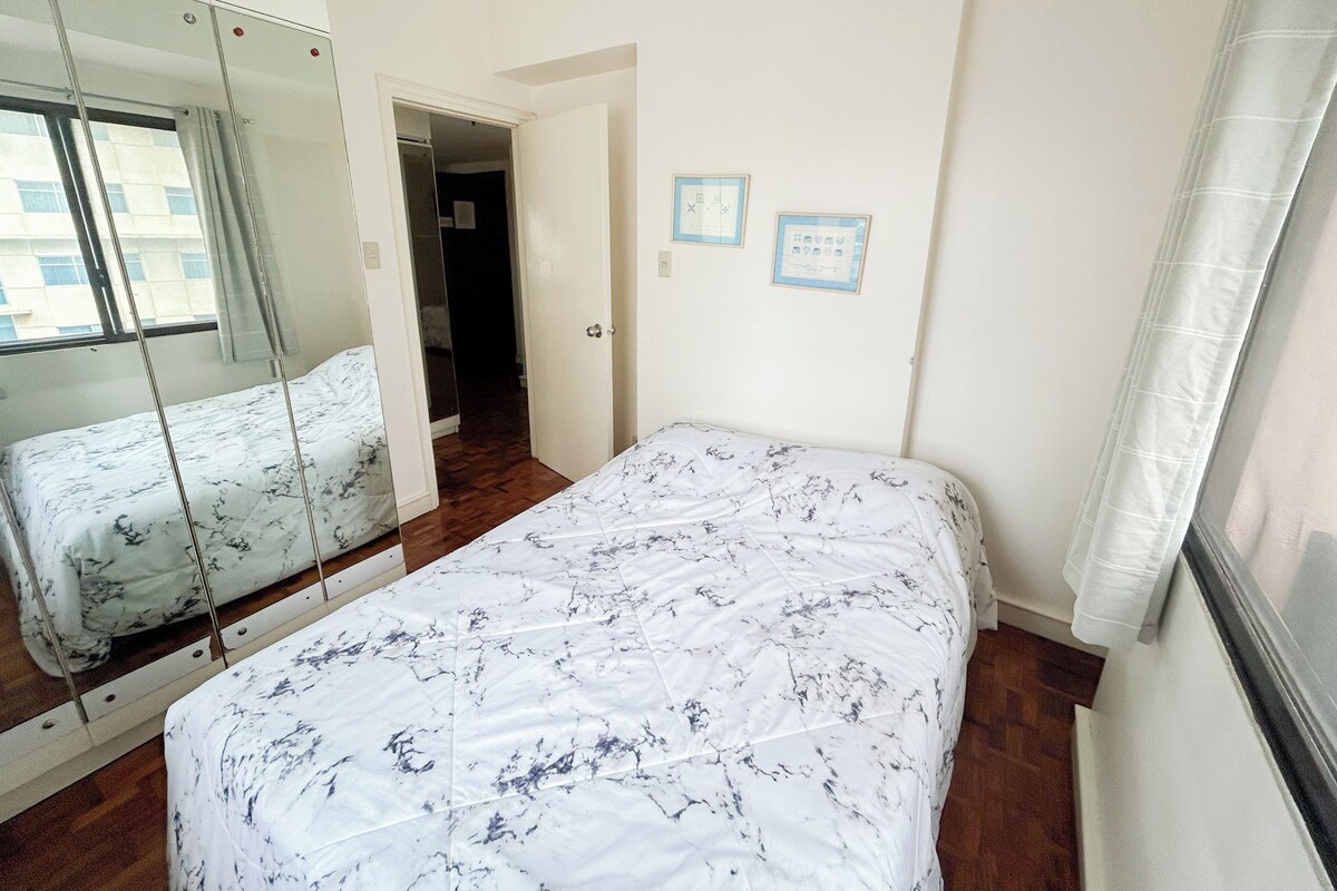 A bedroom with a bed, a mirror, and a door leading to another room.