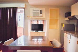 Um espaço de estar compacto com mesa de jantar de vidro, televisão de tela plana, ar-condicionado embutido e um pequeno espaço para cozinha.