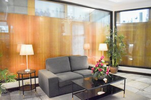 A modern lobby with a grey sofa, two side tables with lamps, a glass coffee table, and a potted plant. - Sunette Tower Suites Makati City Center By Zuzu (Makati)