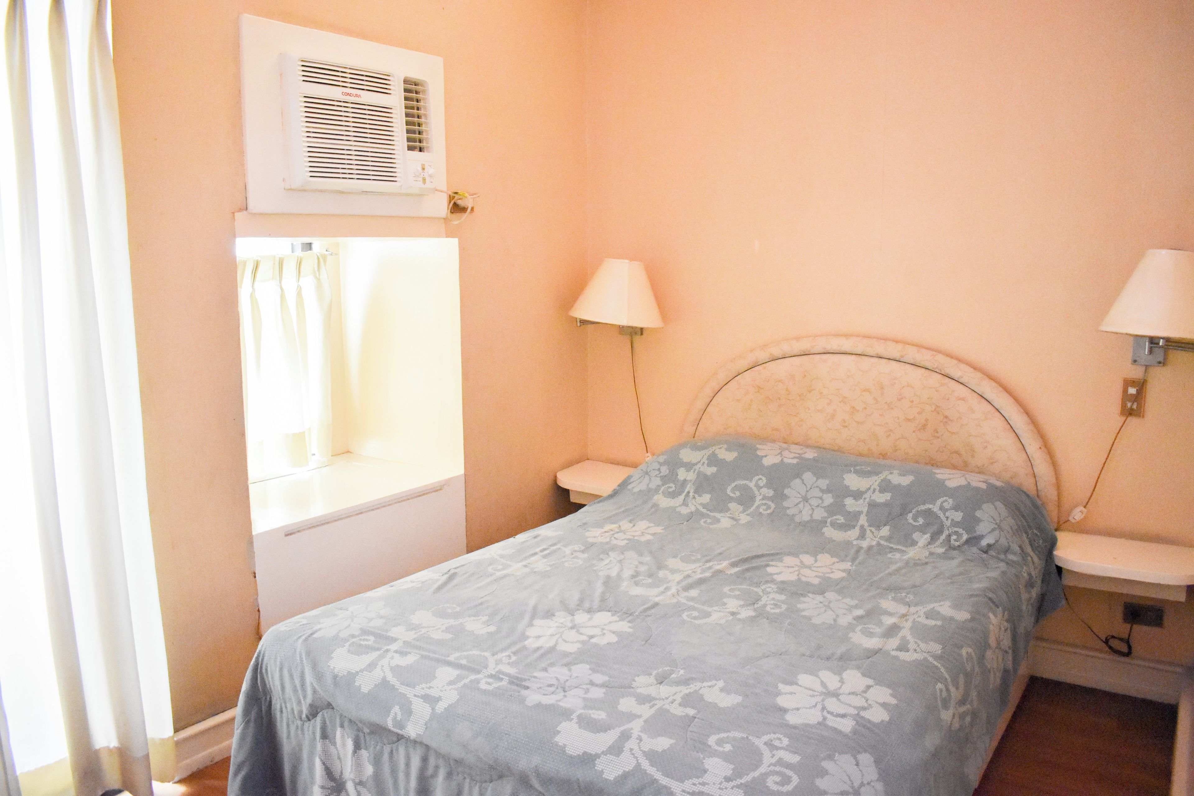 Une chambre à coucher avec un lit, deux lampes de chevet, une fenêtre avec des rideaux et un appareil de climatisation.