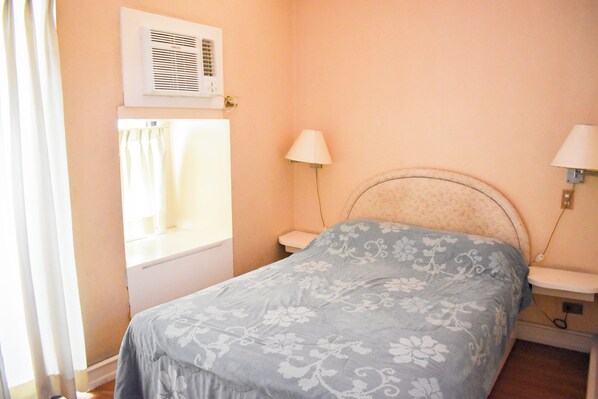 A bedroom with a bed, two bedside lamps, a window with curtains, and an air conditioning unit. - Sunette Tower Suites Makati City Center By Zuzu (Makati)