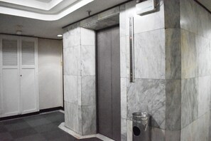 Een moderne lift met een metalen afwerking, een metalen prullenbak en een witte deur met een handgreep.