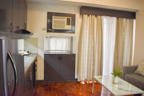 A compact kitchen with a built-in oven, a small window with curtains, and a dining area with a glass table and a plant. - Sunette Tower Suites Makati City Center By Zuzu (Makati)