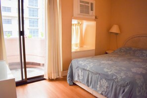 A bedroom with a bed, a window with curtains, an air conditioning unit, and a view of a building outside. - Sunette Tower Suites Makati City Center By Zuzu (Makati)