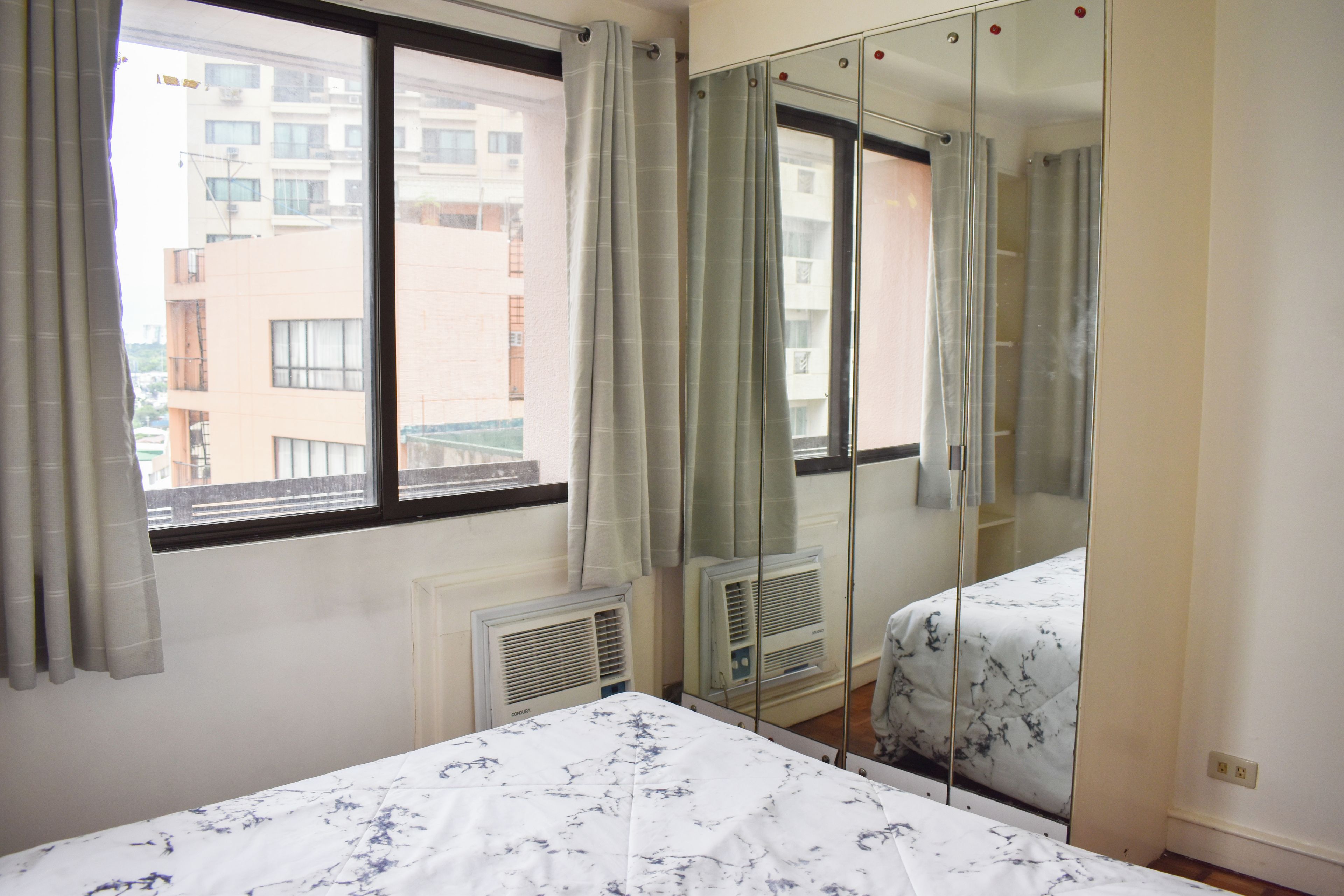Une chambre à coucher avec un lit, une fenêtre avec des rideaux, un radiateur et un miroir.