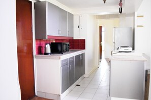 A compact kitchen with grey cabinets, a microwave, and a toaster. - Sunette Tower Suites Makati City Center By Zuzu (Makati)