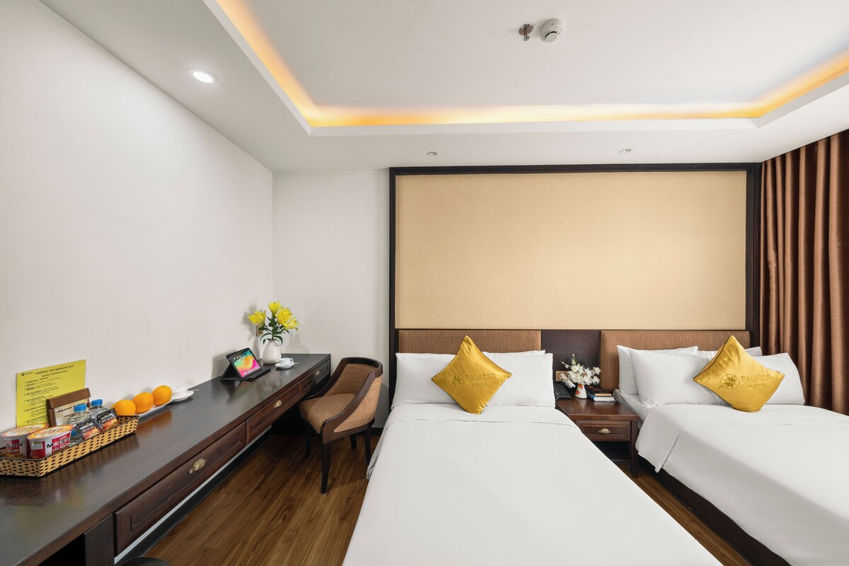 A hotel room with two beds, a desk with a computer, and a chair.