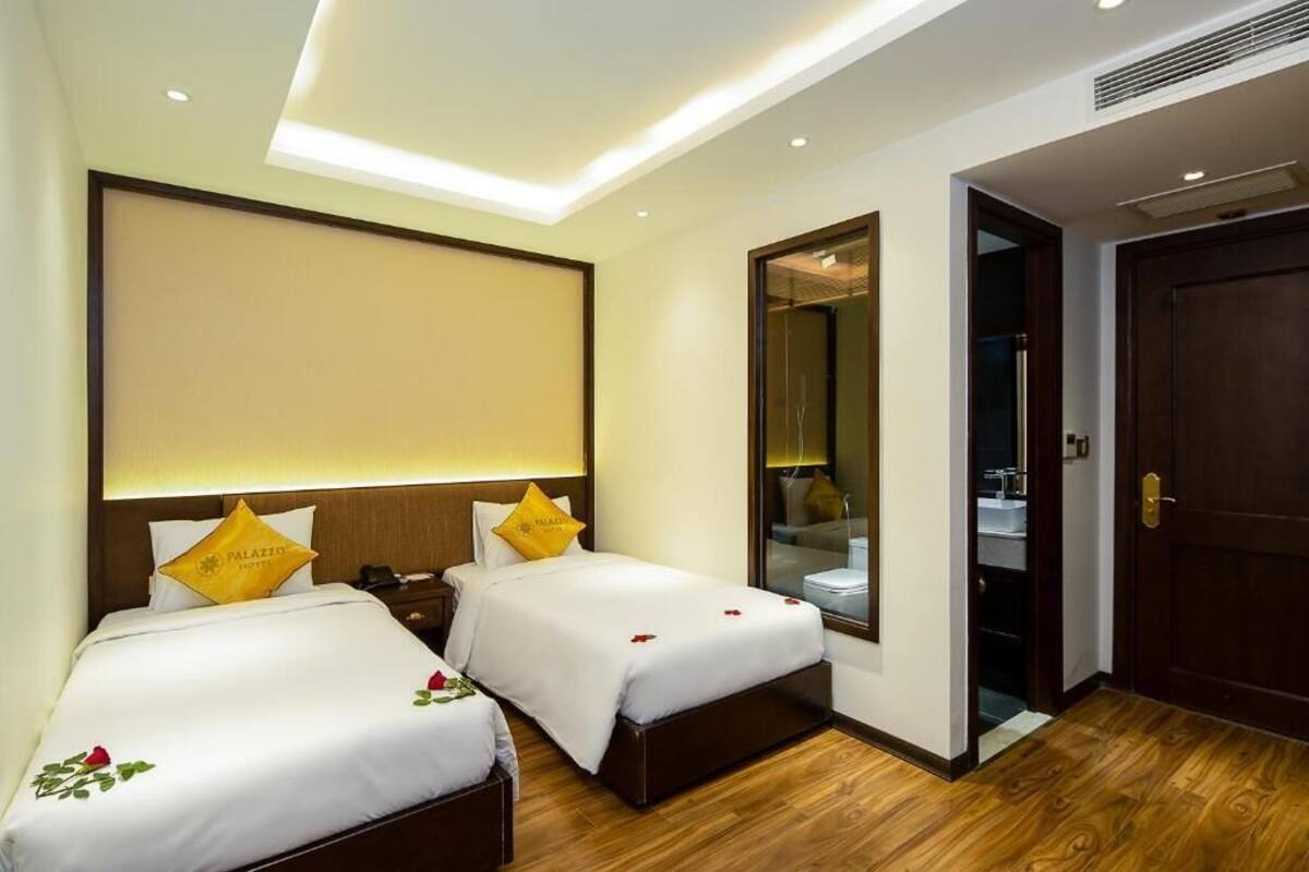 A hotel room with two beds, a large mirror, a wooden floor, and a door to the bathroom.