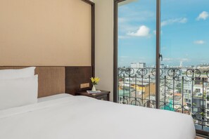 A hotel room with a large bed, a nightstand, and a view of the cityscape through a balcony. - Palazzo 3 (Da Nang Municipality)