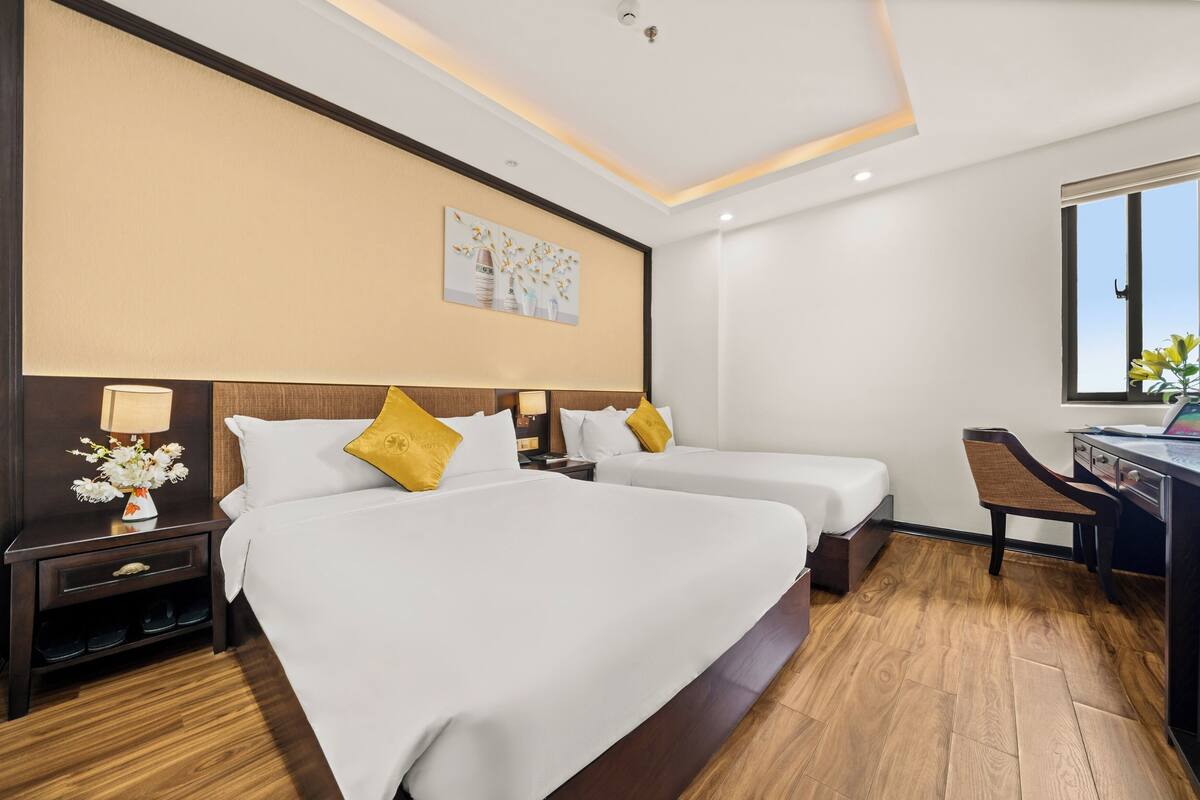 A hotel room with two beds, a desk, and a window.