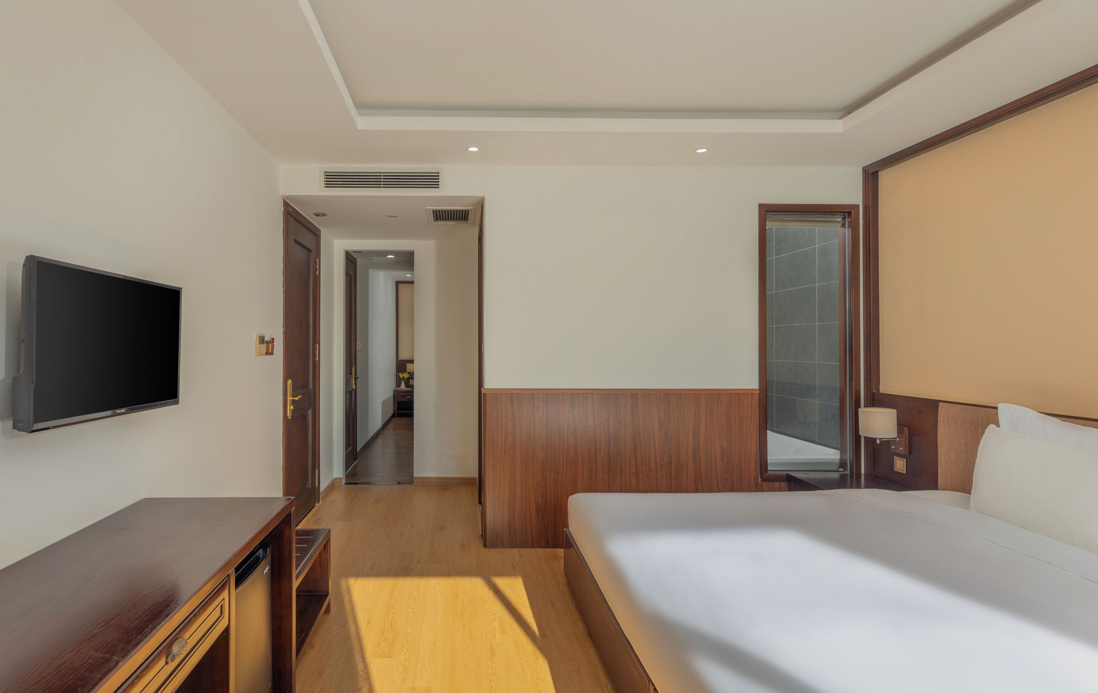 Camera d'albergo con un letto, una TV, un comò in legno, uno specchio e un corridoio che porta al bagno.