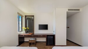 A hotel room with a wooden desk, a small refrigerator, a TV mounted on the wall, and two beds. - Palazzo 3 (Da Nang Municipality)