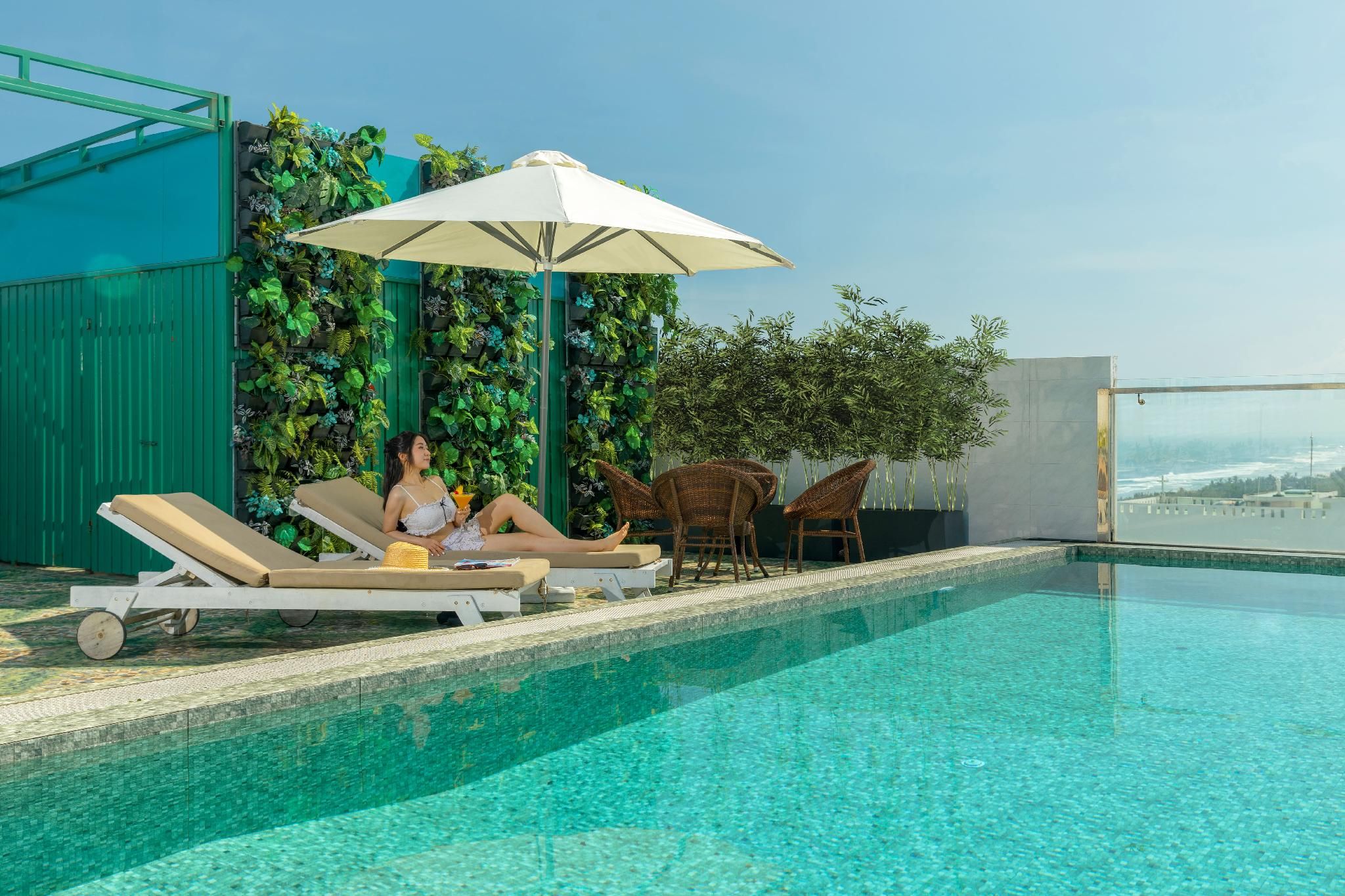 Uma área à beira da piscina com espreguiçadeiras, guarda-sol e vista para a cidade.