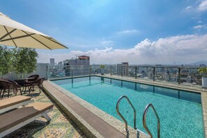 A rooftop pool with clear blue water, surrounded by a glass railing, and overlooking a cityscape with buildings and a mountain in the distance. - Palazzo 3 (Da Nang Municipality)