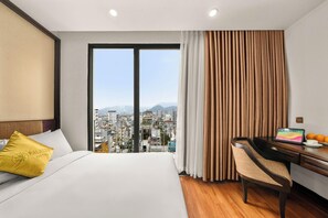 A hotel room with a bed, a desk with a laptop, and a view of a cityscape through large windows. - Palazzo 3 (Da Nang Municipality)