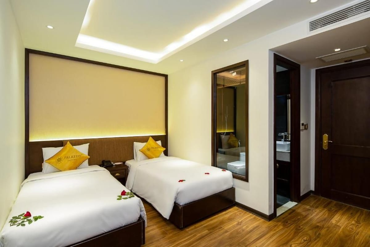 Une chambre d’hôtel avec deux lits, un grand miroir, un plancher en bois et une porte donnant sur la salle de bain.