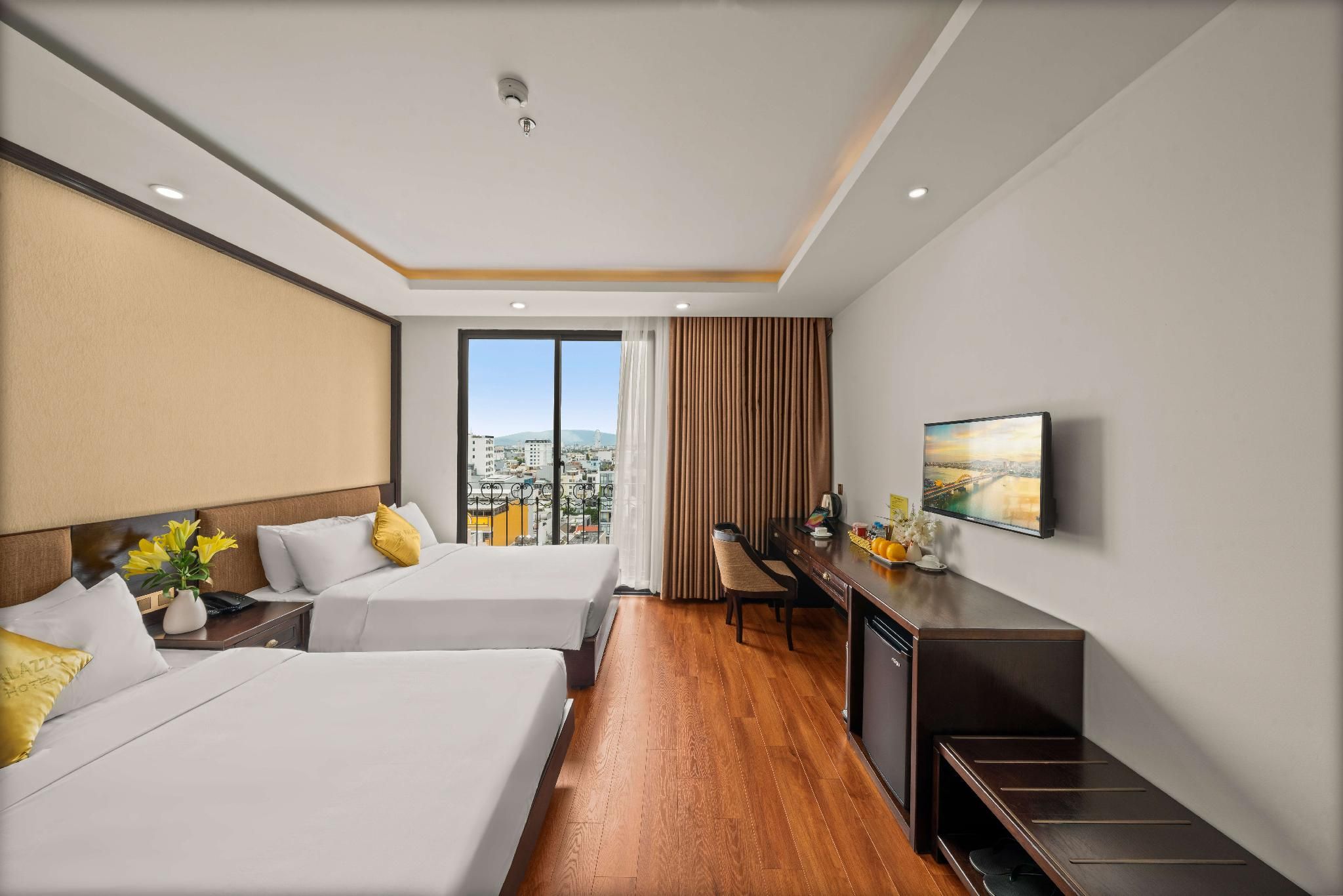 Quarto de hotel com duas camas, uma escrivaninha, televisão e vista para a cidade.