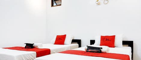 A hotel room with two beds, each with white bedding and red accents. There is a small window and a wall-mounted air conditioning unit.